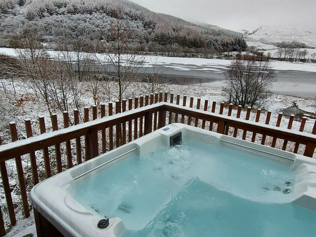 A hot tub on a deck with a view of a snowy landscape.