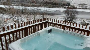 A hot tub on a deck with a view of a snowy landscape.