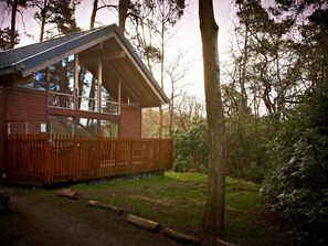 A cabin with a sloped roof, large windows, and a wooden deck. - Strathyre, Ben Ledi - Forest Holidays (Callander)