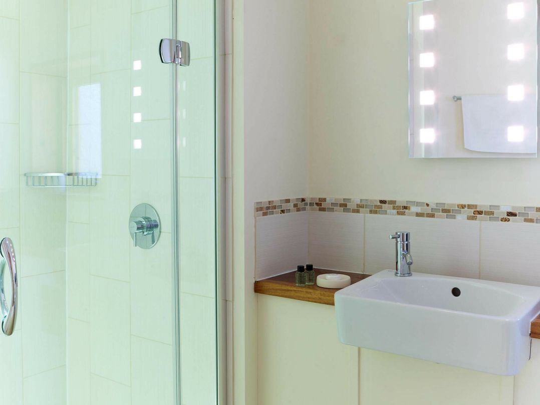 A bathroom with a glass shower enclosure, a sink with a mirror above, and a tiled backsplash.