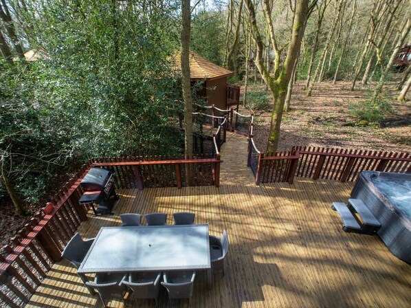 A deck with a table and chairs, surrounded by a wooden fence, leading to a hot tub area.