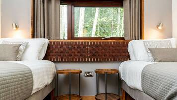 A bedroom with two beds, a window with curtains, a brick-patterned headboard, and two small wooden tables.