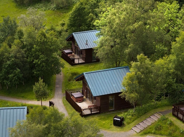 Two cabins with metal roofs, surrounded by dense greenery, connected by a gravel path.