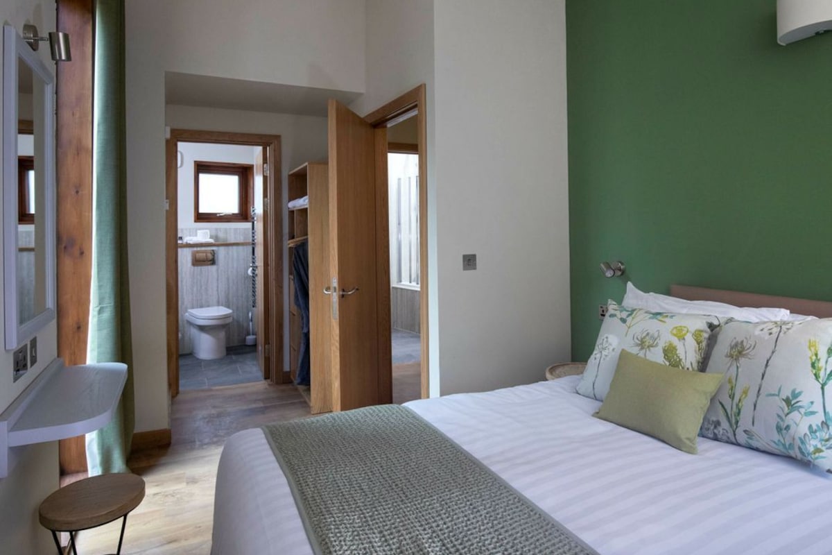 A bedroom with a bed, a bedside table, a chair, a wardrobe, and a bathroom visible through an open door.