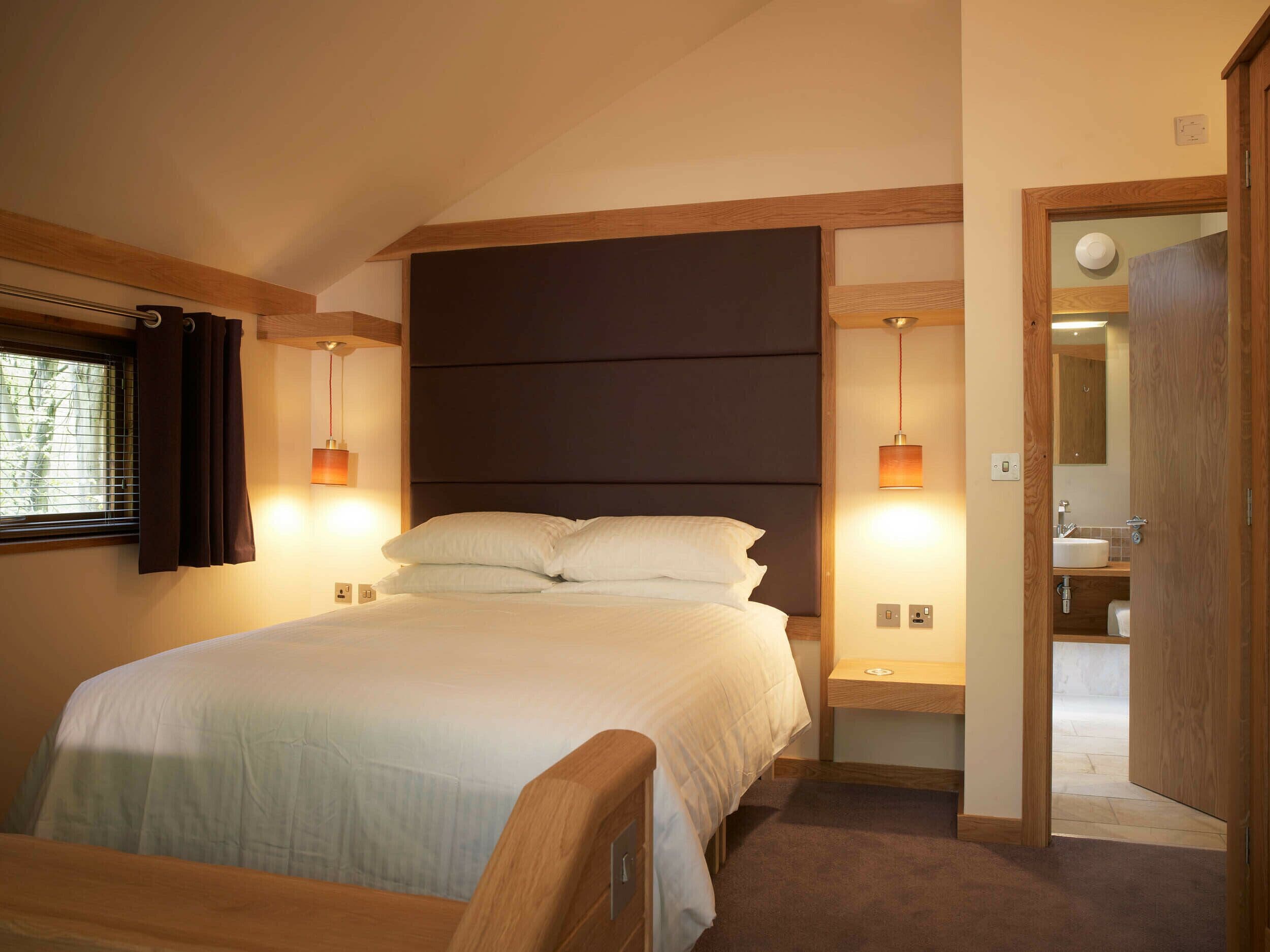 A bedroom with a large bed, bedside lamps, a window with curtains, and a view into the bathroom.