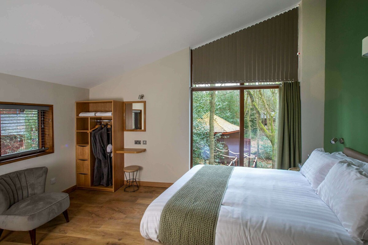 Un dormitorio con cama, una silla, un armario y una ventana con vistas a árboles y un edificio.