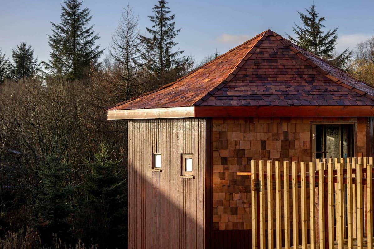 A small wooden cabin with a sloped roof, surrounded by trees.