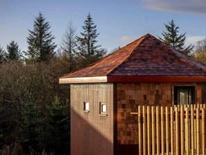 A small wooden cabin with a sloped roof, surrounded by trees.