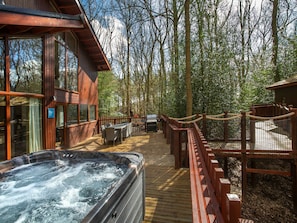 Una terraza de madera con un jacuzzi, mobiliario exterior y una valla de madera.