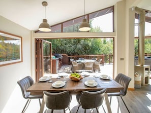 Comedor con mesa de madera dispuesta para cuatro personas, rodeada de sillas y vista a un jardín a través de puertas de cristal grandes.