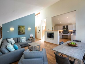 A modern living room with a grey sofa, a dining table with chairs, and a kitchen area in the background. - Garwnant Brecon Beacons- Forest Holidays (Merthyr Tydfil)