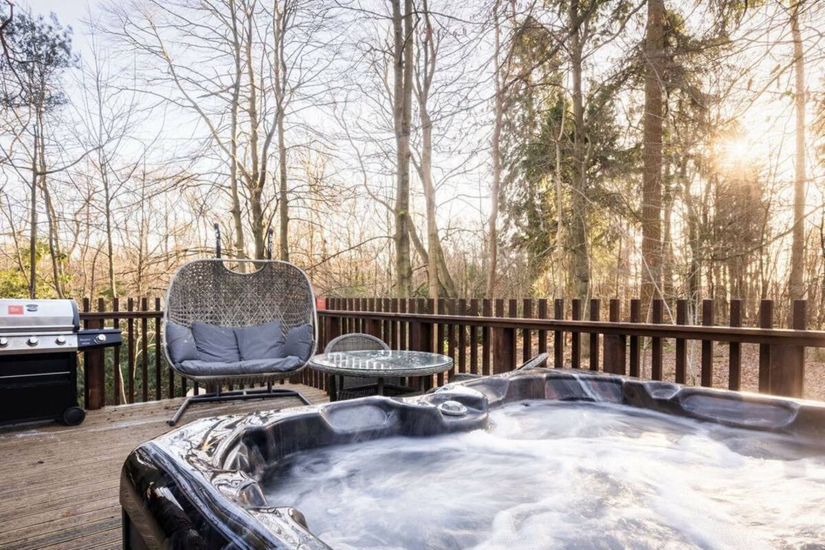 A hot tub on a wooden deck with a grill and seating area.