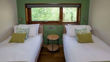 A room with two beds, a small round table, a window with a view of greenery, and a green wall.