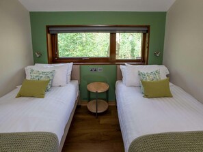 Quarto com duas camas, uma mesa redonda pequena, janela com vista para áreas verdes e parede verde.