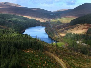 Un paysage pittoresque avec une rivière, des collines boisées et une route sinueuse.