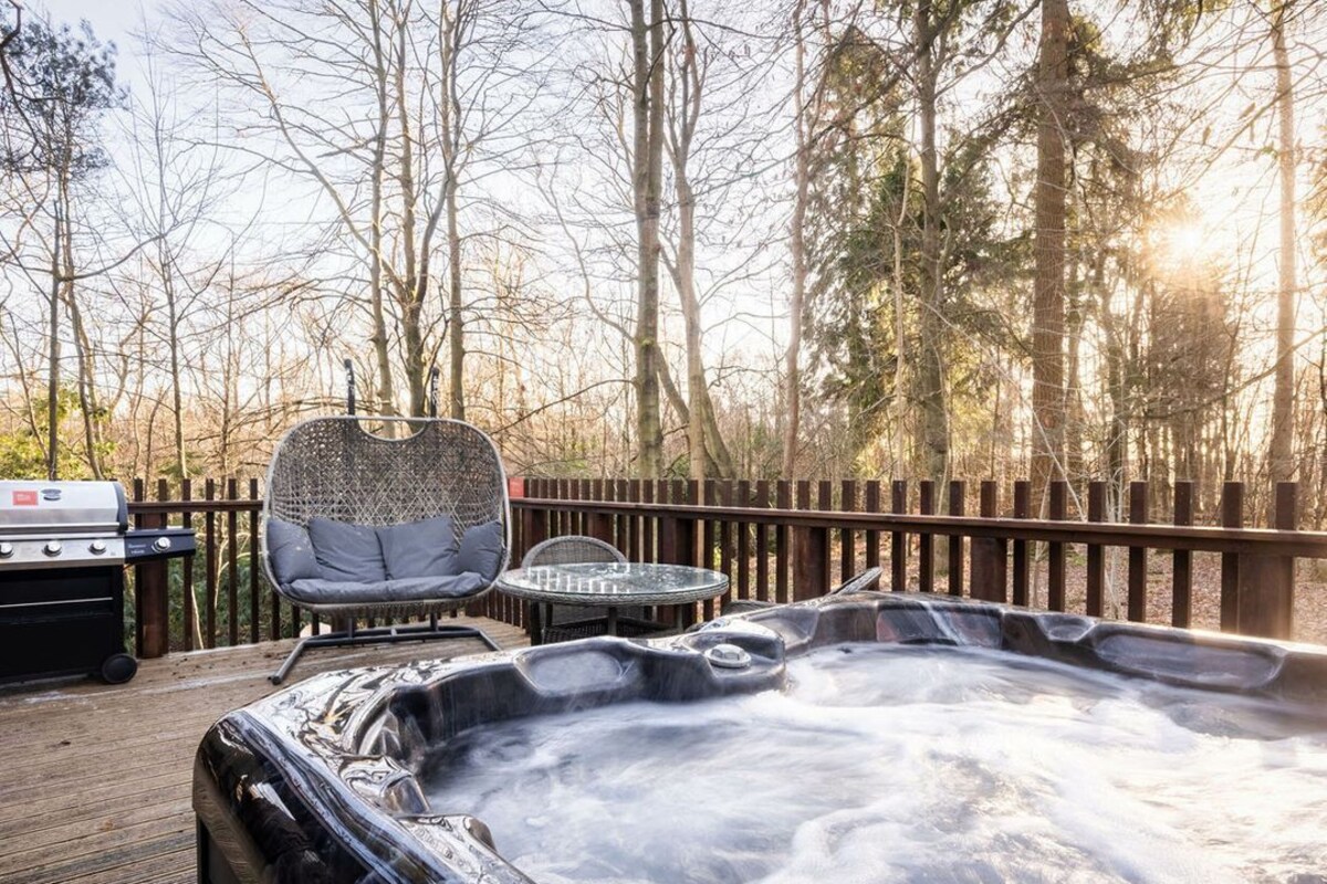 A hot tub on a wooden deck with a grill and seating area.