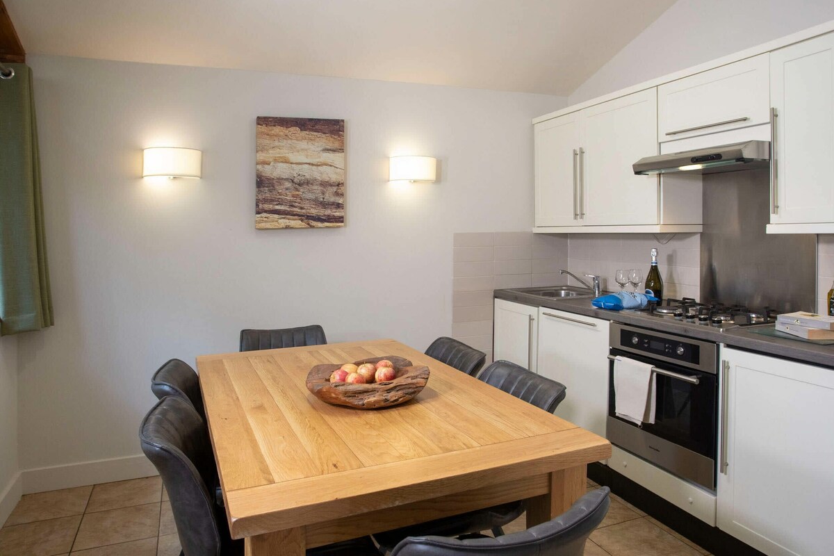 A modern kitchen with white cabinets, a stainless steel range hood, and a dining table with chairs.