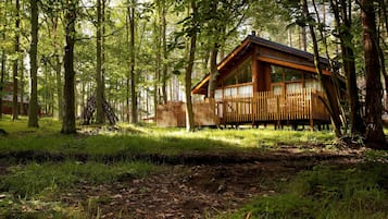 A cabin in a forest with a wooden deck and large windows.
