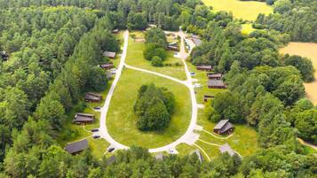 An aerial view of a campground with multiple cabins, a central gathering area, and surrounding forested landscape.