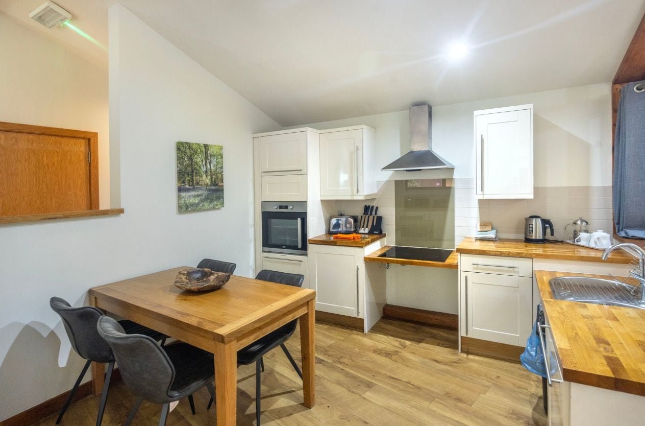 A compact kitchen with white cabinets, a wooden dining table, and a built-in oven.