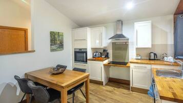 A compact kitchen with white cabinets, a wooden dining table, and a built-in oven.
