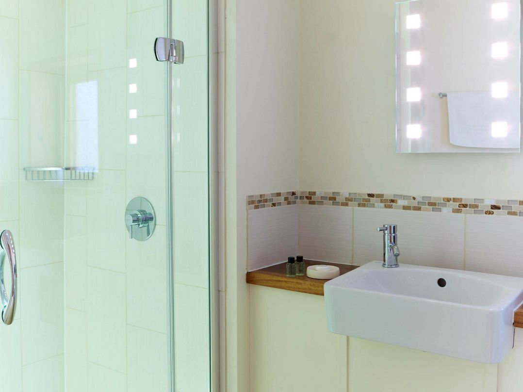 A bathroom with a glass shower enclosure, a sink with a mirror above, and a tiled backsplash.