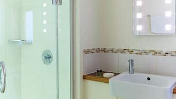 A bathroom with a glass shower enclosure, a sink with a mirror above, and a tiled backsplash.