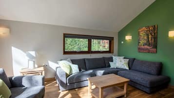 Ein modernes Wohnzimmer mit einem grauen Ecksofa, einem Holztisch und einer grünen Akzentwand.