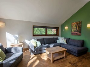 Uma sala de estar moderna com um sofá modular cinza, uma mesa de centro de madeira e uma parede de destaque verde.
