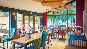 A restaurant with wooden tables and chairs, large windows, and a view of the outdoors.