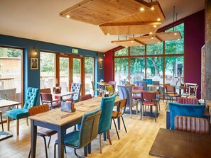 Restaurante com mesas e cadeiras de madeira, grandes janelas e vista para o exterior.