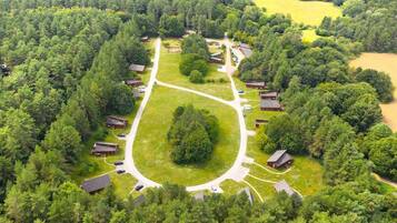 An aerial view of a campground with multiple cabins, a central grassy area, and surrounding dense forest.