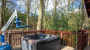 Un bain à remous sur une terrasse en bois avec une rambarde rouge, entouré d’arbres.