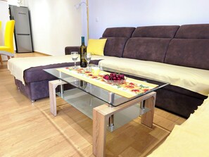 Ein modernes Wohnzimmer mit einem Glastisch, einer Couch, einem Bett und einem kleinen Tisch mit einer Flasche und Gläsern.
