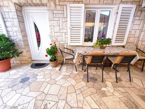 Eine Terrasse mit Tisch, Stühlen, einem Blumentopf und einer Tür mit Fensterläden.