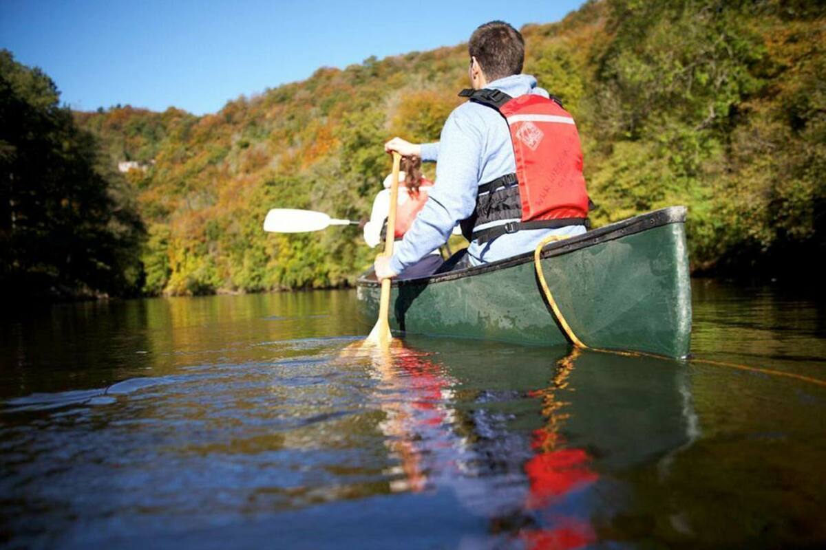 A person in a canoe on a calm river surrounded by greenery.