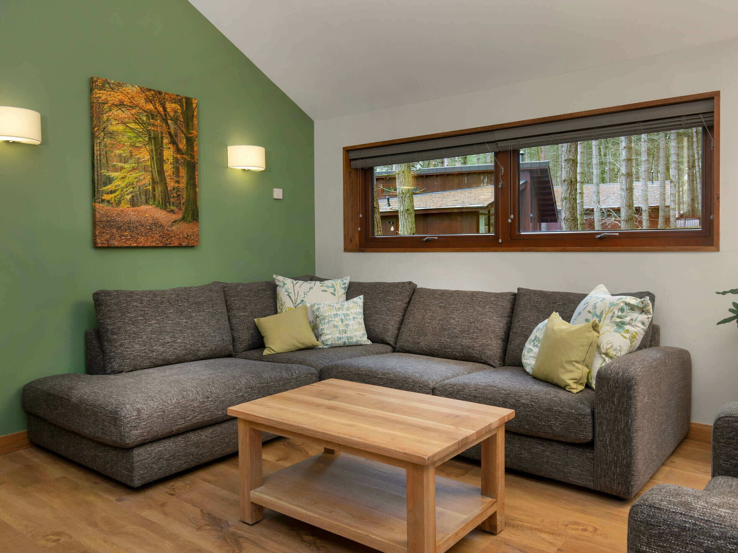 A modern living room with a sectional sofa, a wooden coffee table, and a large window with a view of trees.