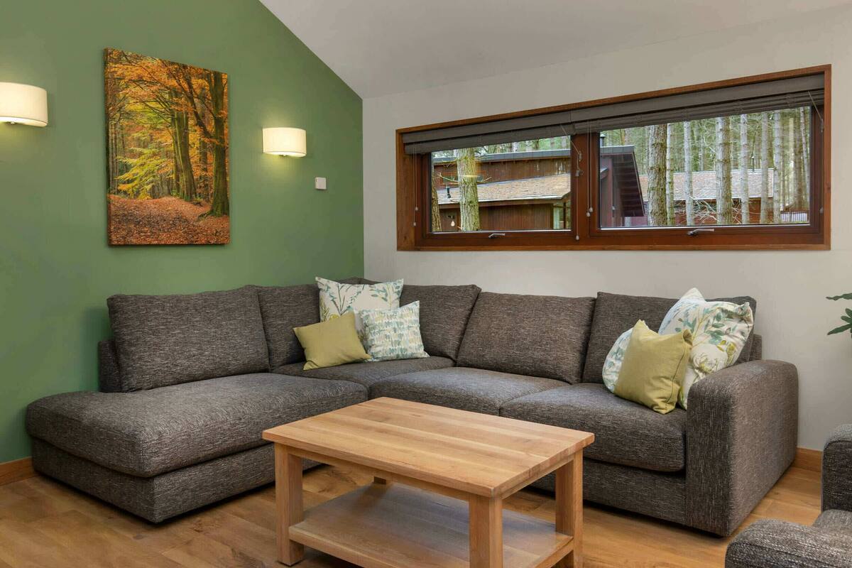 A modern living room with a sectional sofa, a wooden coffee table, and a large window with a view of trees.