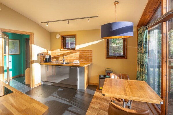 Una cocina moderna con una isla central, un área de comedor con mesa de madera y ventanas amplias que ofrecen luz natural.