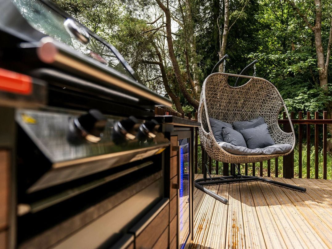 A barbecue grill with a hanging chair and a wooden deck.