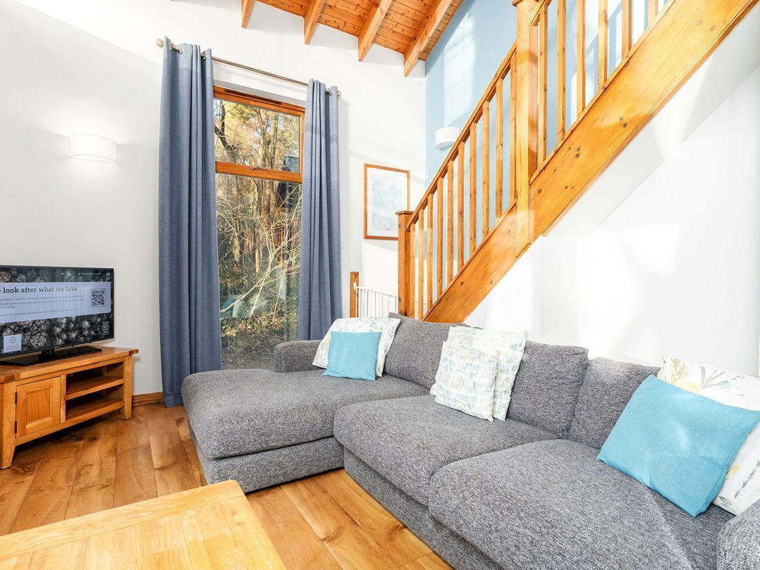 A living room with a grey sectional sofa, wooden flooring, a wooden staircase, and a window with curtains.