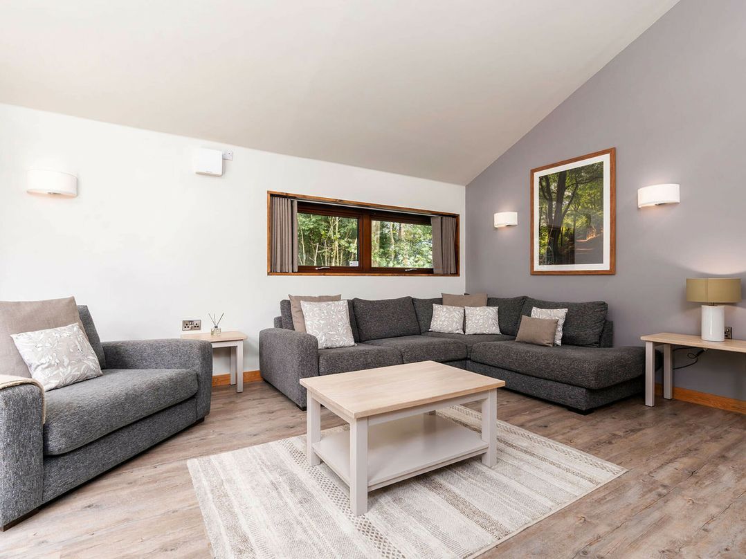 A modern living room with a grey sofa set, a wooden coffee table, and a large window with curtains.