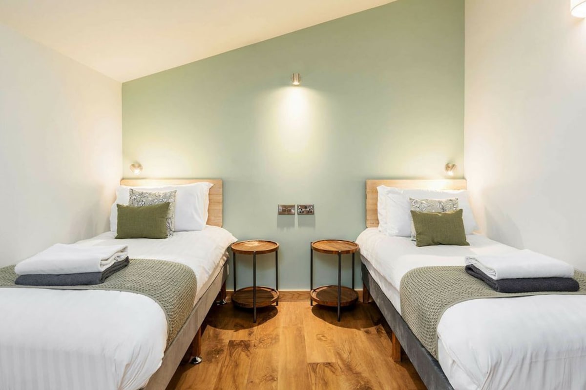 A hotel room with two single beds, a wooden floor, and a light green accent wall.