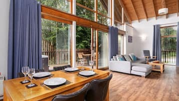 A dining area with a wooden table set for two, a sofa, and a view of the outdoors.