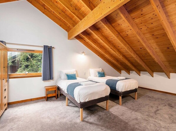 Un dormitorio con dos camas, una ventana con cortinas, techo de madera y una mesita de noche pequeña.