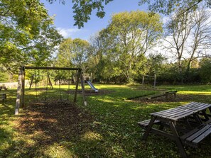 Un parque con un columpio, un tobogán y mesas de picnic.