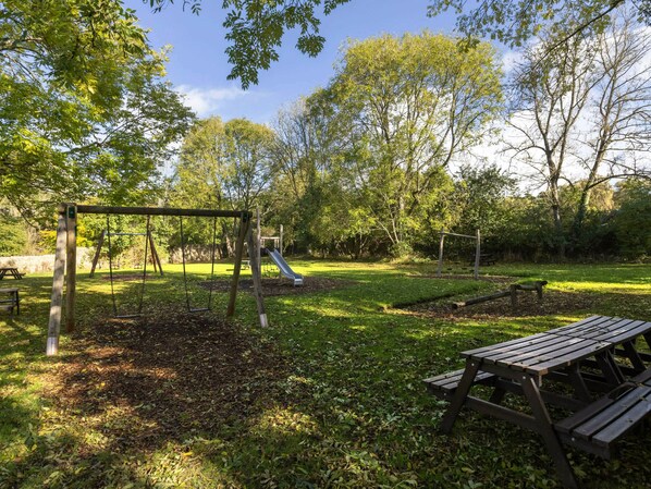 Un parque con un columpio, un tobogán y mesas de picnic.