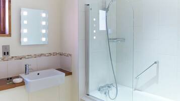 A modern bathroom with a glass-enclosed shower, a white sink with a mirror, and a tiled wall.