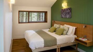 A bedroom with a bed, a window, a wall-mounted light, and a bedside table with a book.