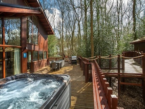 A wooden deck with a hot tub, outdoor furniture, and a barbecue area surrounded by a wooden fence.